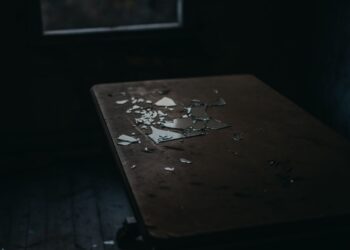 A moody shot of broken glass pieces scattered on an old wooden table in a dimly lit room.