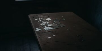 A moody shot of broken glass pieces scattered on an old wooden table in a dimly lit room.