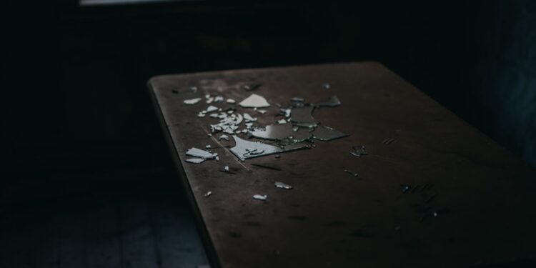 A moody shot of broken glass pieces scattered on an old wooden table in a dimly lit room.