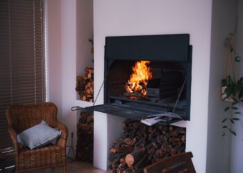 A warm and inviting indoor fireplace with stacked firewood, wicker chair, and plants for a cozy ambiance.