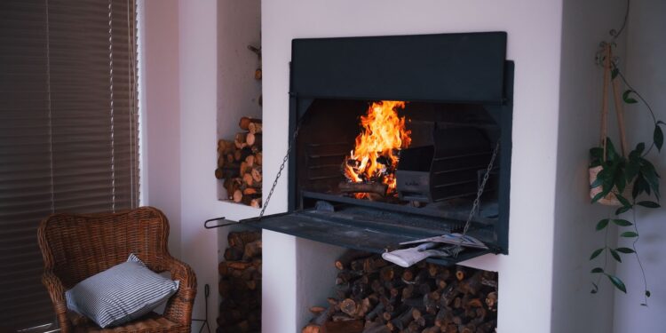 A warm and inviting indoor fireplace with stacked firewood, wicker chair, and plants for a cozy ambiance.