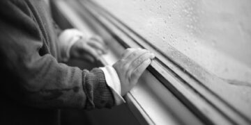 A child's hand touching a rainy window, expressing curiosity and solitude.