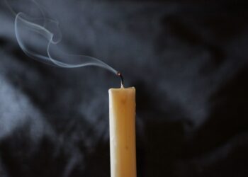 A wick's smoke trails from a recently extinguished candle on dark background.