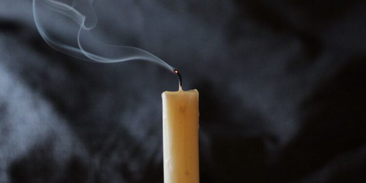 A wick's smoke trails from a recently extinguished candle on dark background.