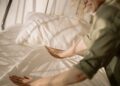 A person arranging bed linens in a warm, sunlit bedroom, creating a cozy and inviting atmosphere.