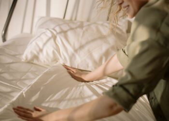 A person arranging bed linens in a warm, sunlit bedroom, creating a cozy and inviting atmosphere.