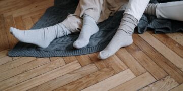 A couple wearing socks, relaxing on a wooden floor with a gray blanket, enjoying warmth.