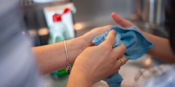 Detailed image of two people cleaning using a blue cloth indoors. Perfect for hygiene concepts.