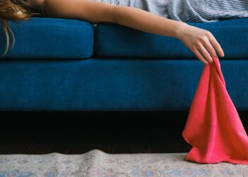 Crop unrecognizable female with dusting cloth in hand lying on sofa while resting after cleaning apartment