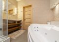 Interior of modern bathroom with shower near bath and sink on cabinet under mirror next to door