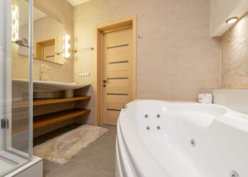Interior of modern bathroom with shower near bath and sink on cabinet under mirror next to door