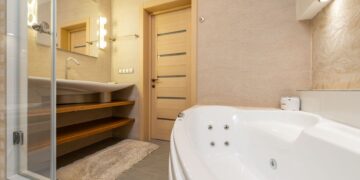 Interior of modern bathroom with shower near bath and sink on cabinet under mirror next to door