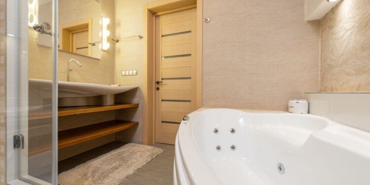 Interior of modern bathroom with shower near bath and sink on cabinet under mirror next to door