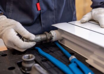 Close-up of a plumber installing a radiator pipe using specialized tools.