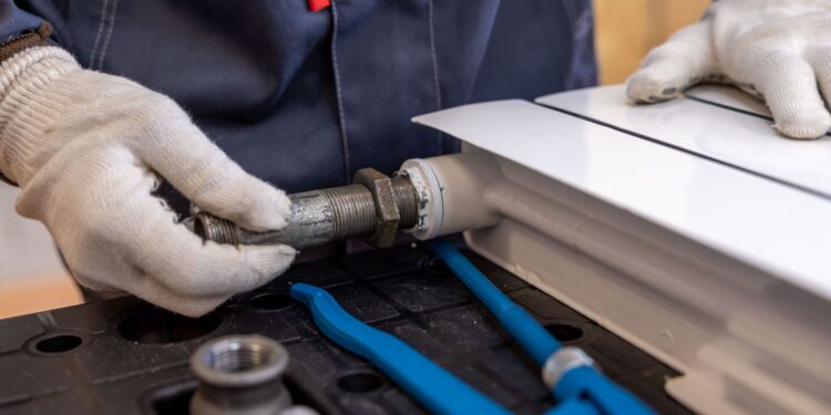 Close-up of a plumber installing a radiator pipe using specialized tools.