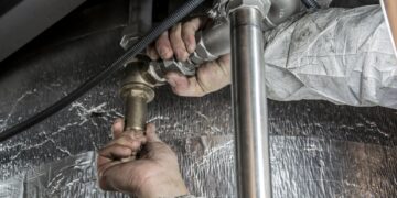 Close-up of a plumber's hands installing steel pipes indoors, showcasing skilled manual work.