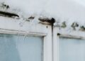 Sharp icicles hang from a window frame, covered in snow, showcasing winter's beauty.
