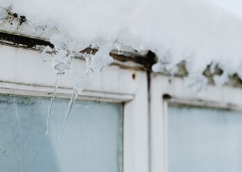 Sharp icicles hang from a window frame, covered in snow, showcasing winter's beauty.