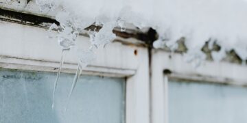 Sharp icicles hang from a window frame, covered in snow, showcasing winter's beauty.