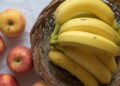 A close-up of ripe bananas in a wicker basket with apples on a white background.