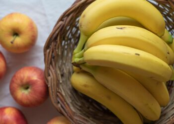 A close-up of ripe bananas in a wicker basket with apples on a white background.