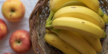 A close-up of ripe bananas in a wicker basket with apples on a white background.