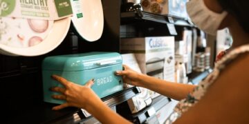 A woman shopping for a turquoise bread bin in a store while wearing a face mask.
