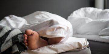 A close-up of a bare foot poking out from under a soft duvet in a modern bedroom.