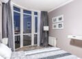 Elegant bedroom with large windows overlooking city lights, featuring a stylish decor and a cozy ambiance.