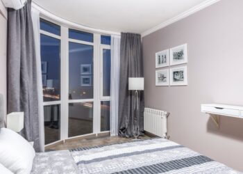 Elegant bedroom with large windows overlooking city lights, featuring a stylish decor and a cozy ambiance.