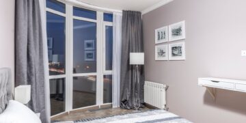 Elegant bedroom with large windows overlooking city lights, featuring a stylish decor and a cozy ambiance.