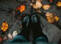 Two black boots on a leaf-covered, wet stone path, capturing the essence of autumn.