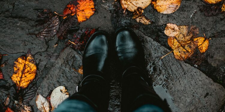 Two black boots on a leaf-covered, wet stone path, capturing the essence of autumn.