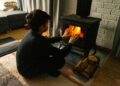 A child warms hands by a wood stove in a cozy living room, creating a warm winter ambiance.