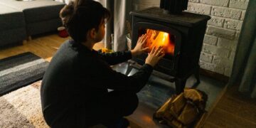 A child warms hands by a wood stove in a cozy living room, creating a warm winter ambiance.