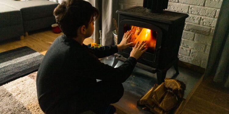A child warms hands by a wood stove in a cozy living room, creating a warm winter ambiance.