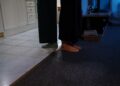 A close-up of feet standing on carpet and tile flooring in a cozy indoor setting.