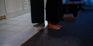 A close-up of feet standing on carpet and tile flooring in a cozy indoor setting.