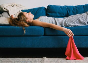Side view of young exhausted woman with rag lying on couch in living room in daylight
